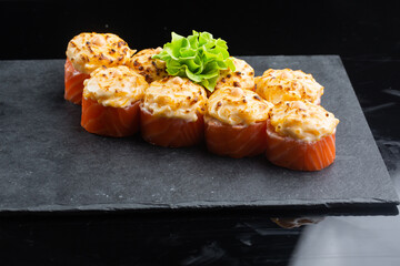 baked sushi with salmon, avocado, red caviar and cream cheese isolated on black background. Delicious traditional Japanese food with sushi rolls. Hot sushi