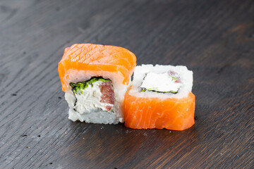 Close-up of uramaki sushi rolls with red caviar, salmon, tuna, cucumber and avocado isolated on black background. Delicious traditional japanese food with sushi rolls.