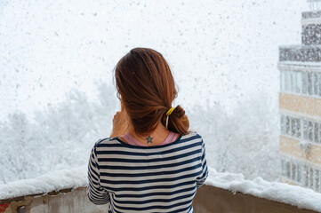 A young girl in a striped sweater stands alone on a balcony