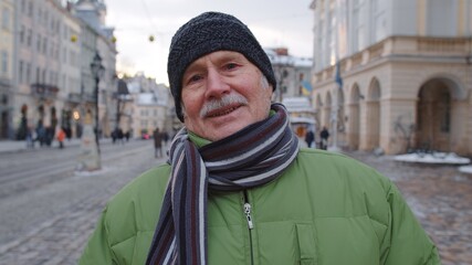 Portrait of stylish senior man grandfather tourist smiling, looking at camera in winter city center...