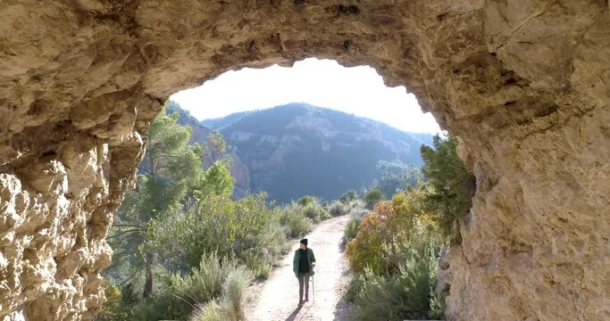 Mujer senderista camina hacia dron entrando en gruta de piedra