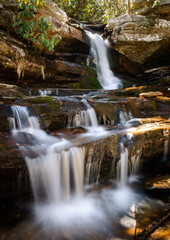 Small waterfall cascades over sunlit rocks in summer forest