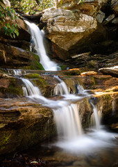 Naklejka na ściany i meble Small waterfall cascades over sunlit rocks in summer forest