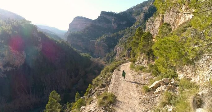 dron vuela sobre mujer que camina por senda de monta&ntilde;a junto a precipicio