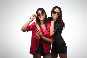 Young twins hugging. Teen twin sisters wearing leather jackets and sunglasses on light background