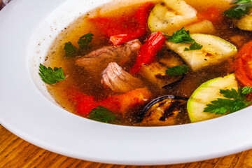 Soup with meat and grilled vegetables in white plate