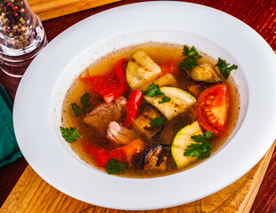 Soup with meat and grilled vegetables in white plate