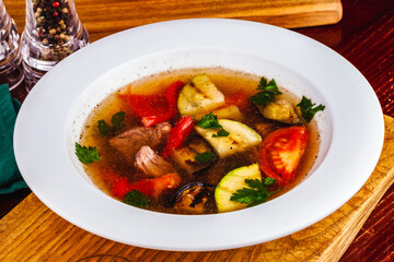 Soup with meat and grilled vegetables in white plate