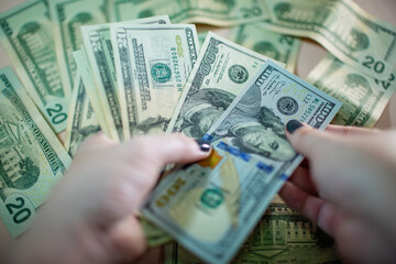Close-up of a hand holding a pile of US banknotes. Cash of one hundred dollar bills. Background of many banknotes