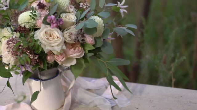 Bouquet of pink and cream roses, eucalyptus twigs, white dahlias and delicate purple flowers in a white vase on the table