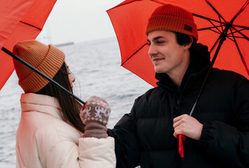 Young hipster couple walking with two red umbrellas in cold weather, love story outdoors