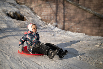 Little girl moving fast from snowy hill on snow sled in winter