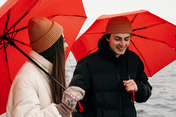 Young hipster couple walking with two red umbrellas in cold weather, love story outdoors