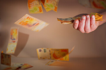 Male hand holding a bundle of money with colorful background. Top view of one thousand Argentine peso bills. banknotes falling background.