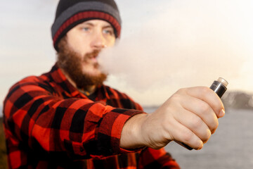 Person holding an electronic cigarette in his hand and exhaling the vapor produced. man vaping....