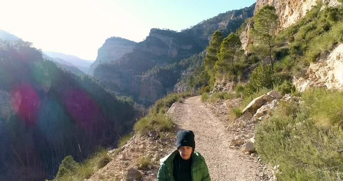 mujer con gorro y abrigo verde pasea por sendero de montaña y dron sobrevuela