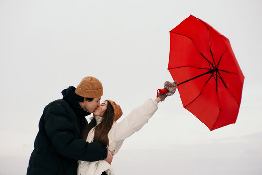 Young hipster couple walking with two red umbrellas in cold weather, love story outdoors - Powered by Adobe