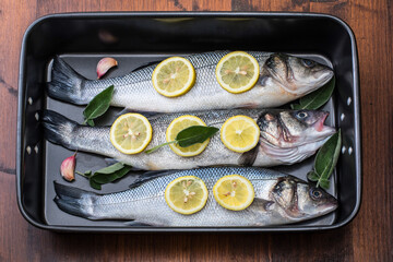 fresh sea bass pready for cooking in the pan with lemon slices and sage