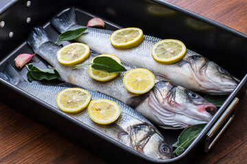 fresh sea bass pready for cooking in the pan with lemon slices and sage