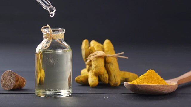 Glass bottle of essential turmeric oil, turmeric powder in wooden spoon and root on rustic background, oil dripping, ( curcuma longa )