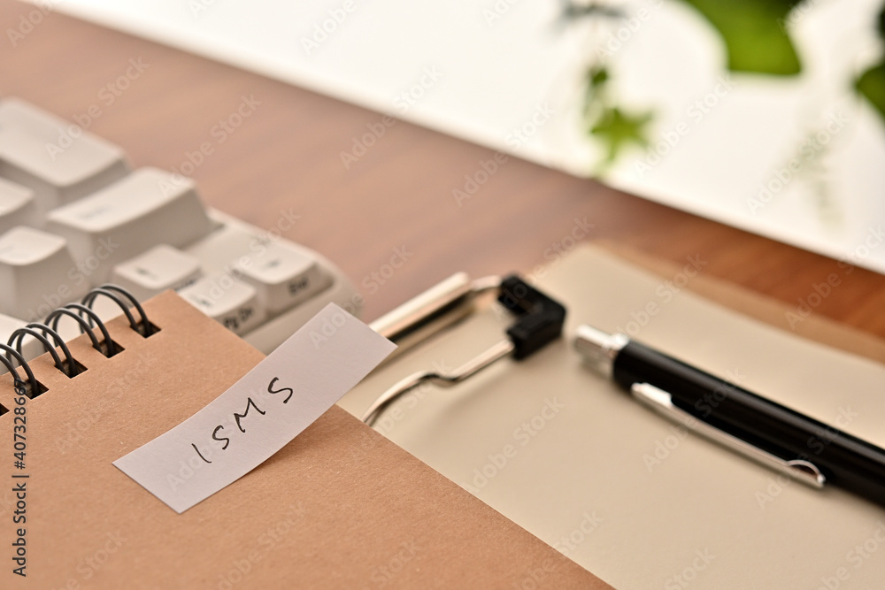 Poster a sticky note labeled isms is taped to the edge of a notebook on the desk.that's an acronym for info