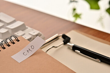 A sticky note labeled CMO is taped to the edge of a notebook on the desk.That's an acronym for...