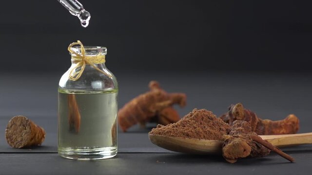 Glass bottle of galangal essential oil, root and galanga powder in wooden spoon on black wooden table, (Alpinia officinarum ), oil dripping
