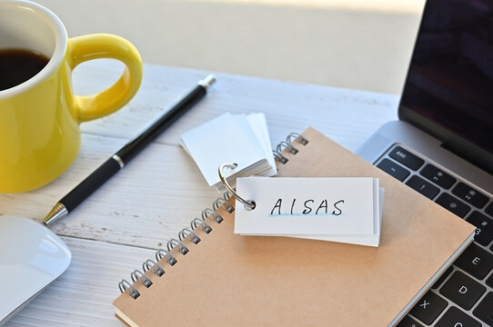 There's a word book on a desk with a cup of coffee and laptop pc. The word AISAS is written in it. It's an abbreviation for Attention, Interes, Search, Action, Share.
