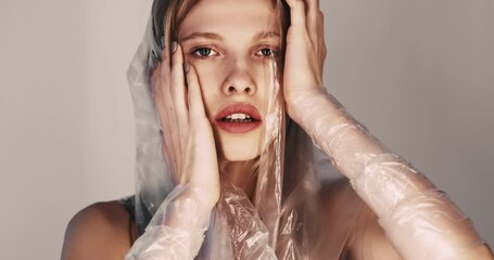 Woman abuse. Domestic violence. Female rights. Art portrait of sensual hurt lady with full lips wearing polyethylene film touching head suffering from humiliation isolated on beige background.