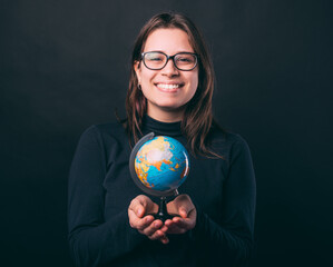 Excited young woman is holding a small Earth globe over black background