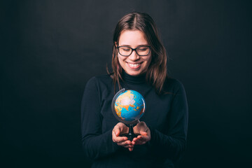 Photo of cute young woman holding globe and smiling over dark background.