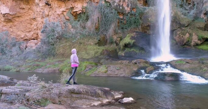 Mujer con capucha rosa cerca de cascada de agua vista a&eacute;rea de dron