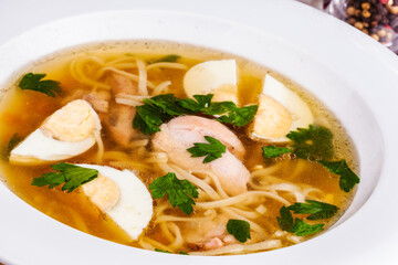Chicken soup with noodles and egg in white plate
