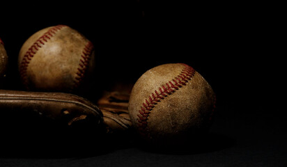 Baseballs and glove in dark moody sports atmosphere with black background.