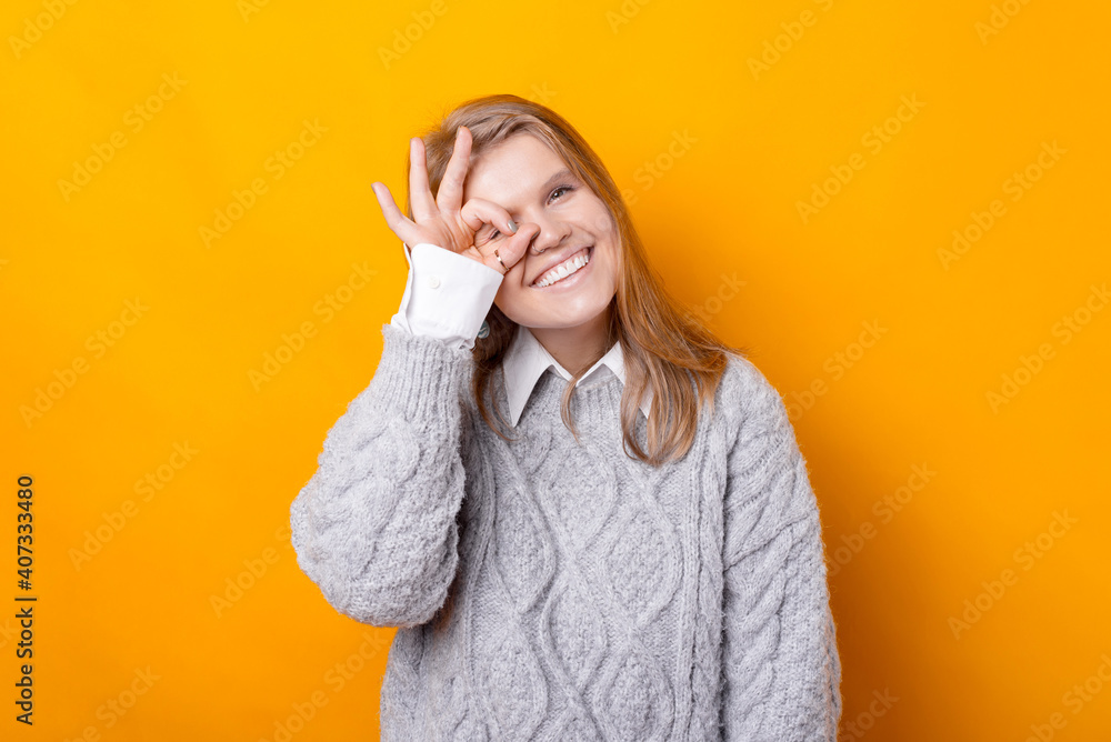 Wall mural photo of cheerful young woman in sweater making ok gesture over yellow background.