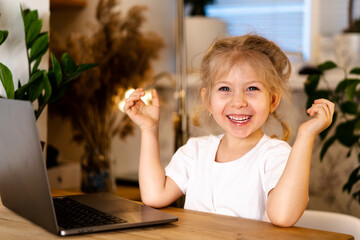 Fototapeta premium a small blonde girl with a laptop sits at a table and smiles
