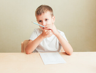 7 years old child boy sitting at desk with sheet of paper and pencil and doing math test