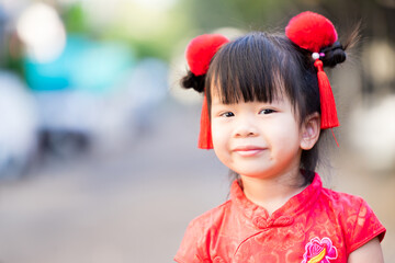 Asian girl dressed in red cheongsam and decorated with fluffy hair clips, with red tassels, to celebrate the Chinese New Year, according to ancestral tradition. Happy child smile sweet, aged 3-4 years