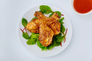Roasted chicken drumsticks with spicy sauce on white background.