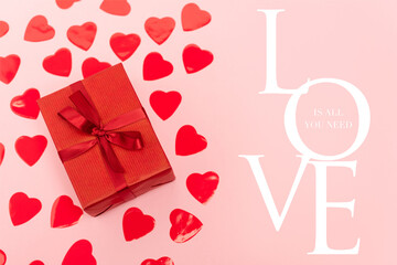 Top view of red hearts and gift box near love is all you need lettering on pink background