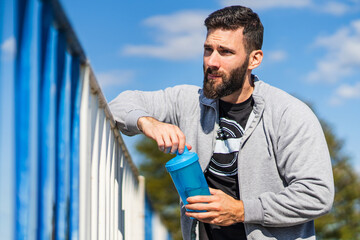 Adult male caucasian athlete standing outdoor opening the bottle of supplement shaker in sunny day...