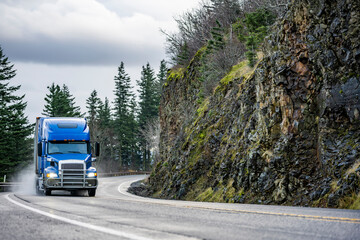 Big rig blue semi truck with grill guard transporting cargo in semi trailer running on the winding...