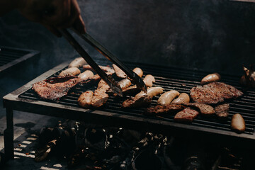 Roasting meat on a grill, hand with tongs turning the meat.