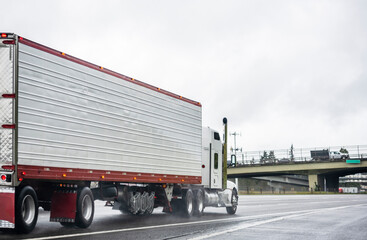 Industrial classic big rig white semi truck transporting cargo in refrigerator semi trailer running...
