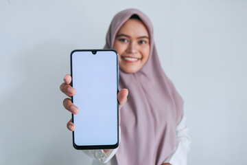 Young Asian Islam woman wearing headscarf is pointing finger on white screen of phone with smile...