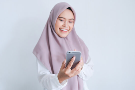 Young Asian Islam woman wearing headscarf is smile and happy in what she see on the smartphone. Indonesian woman on gray background