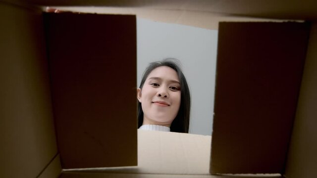 Asian woman excited happy opening unpacking a package parcel with surprised face reaction, shopping purchase from ecommerce online retail store, unpack delivered cardboard box taking out product.