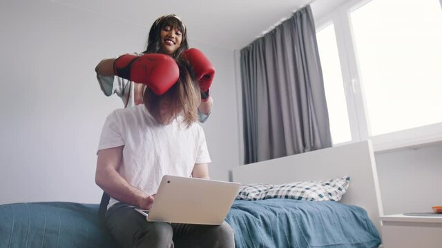 Young Woman Distracting Her Boyfriend From Working On Laptop. Attention Seeker With Boxing Gloves Playing With Partners Long Hair. High Quality 4k Footage