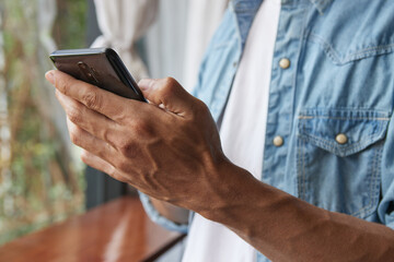 Zoom View Left Hand of Young Asian Casual Businessman in Denim or Jeans Shirt Using Smartphone in Coffee Shop. Casual Businessman Working with Technology
