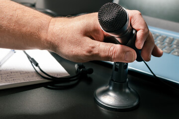 A man's hand accommodating a desktop microphone before a virtual conference. Modern style, Virtual...